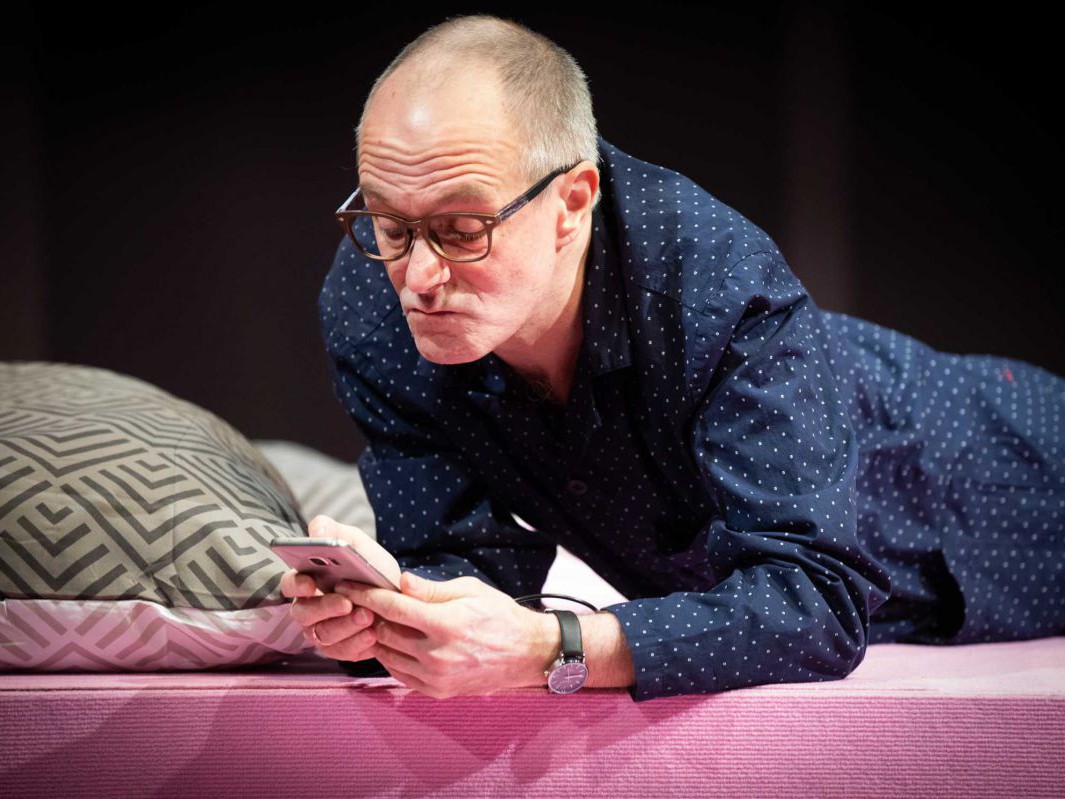 Jens Claßen mit Handy auf Bett, Reigen, TAG Theater Jens Claßen mit Handy auf Bett, Reigen, TAG Theater
